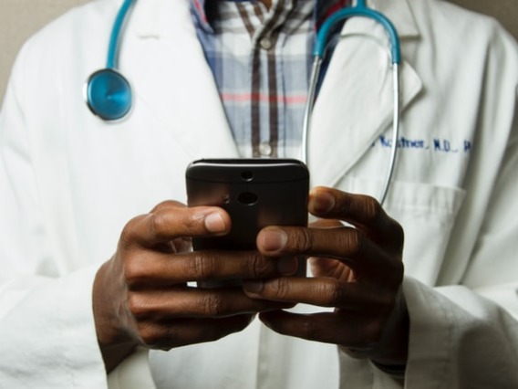 Photo of a black man in a white lab coat holding a phone. 