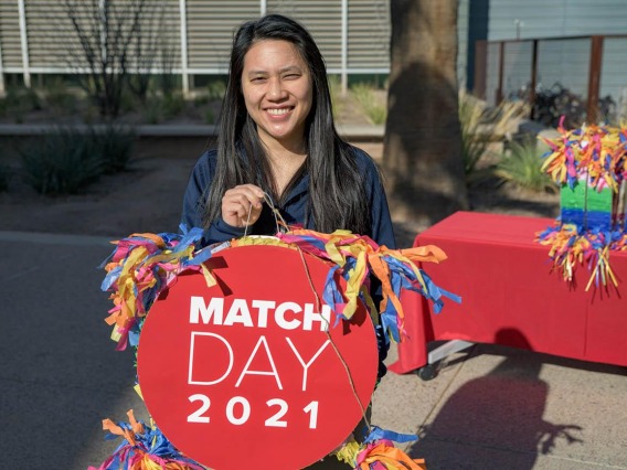 Smiling asian woman holds a red pinata which reads Match Day 2021