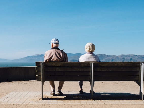 Two elderly people sitting on a bench looking over the horizon with mountains in the distance