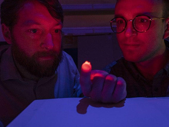 Dr. Philipp Gutruf and Jokubas Ausra dimly lit with a glowing, red optogenetics device