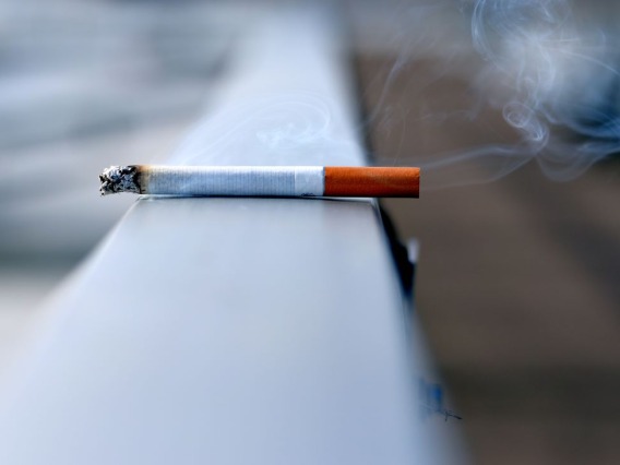 A burning cigarette sits on a hand rail