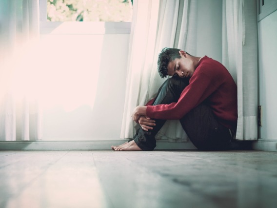 Young person in sweater sits on the ground and hugs his knees to his chest