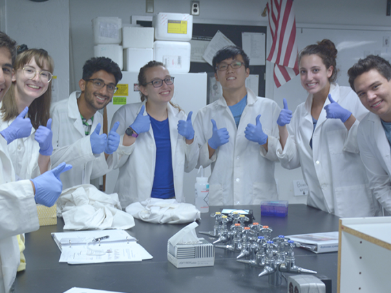 Students in labs coats standing in a group giving thumbs up