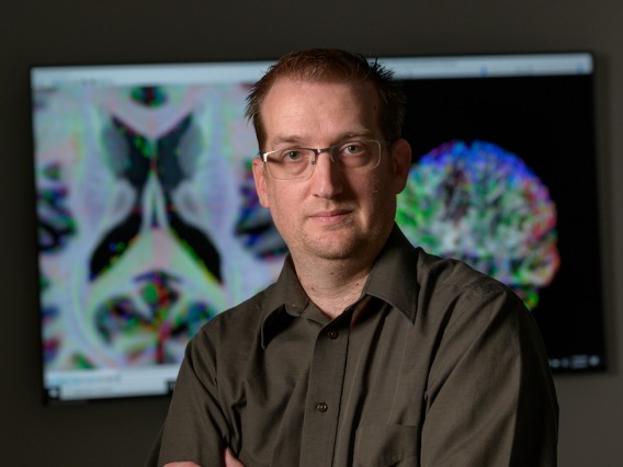 Adam Raikes in front of colorful brain images.