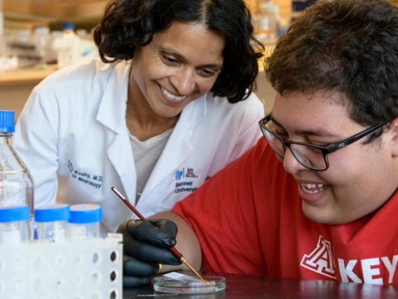 Dr. Anita Koshy wearing a white lab coat, smiling with boy student intern wearing a red tshirt