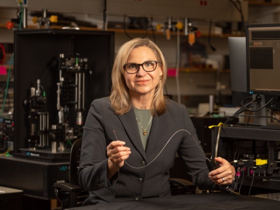 Dr. Jennifer Barton in her lab wearing a dark gray suit jacket and dark glasses holding wire imaging device