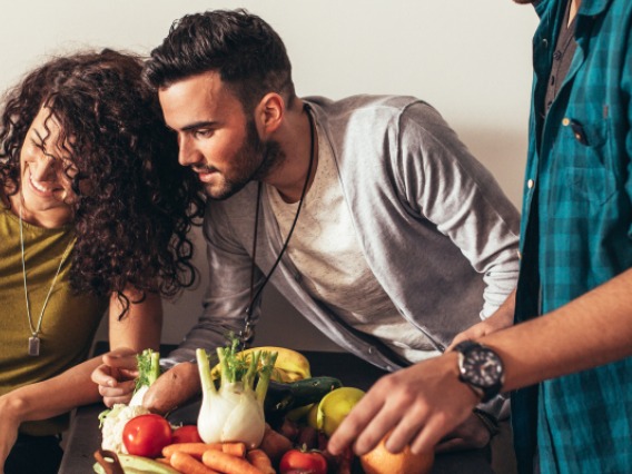 Man and woman looking at a laptop and smiling behind two people handling vegetables