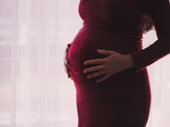 Pregnant woman in a red dress holding belly.
