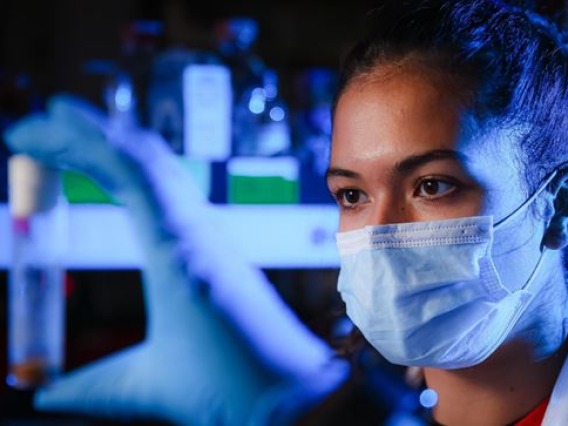 Grace Hala’ufia looking at sample in a lab with blue lighting.