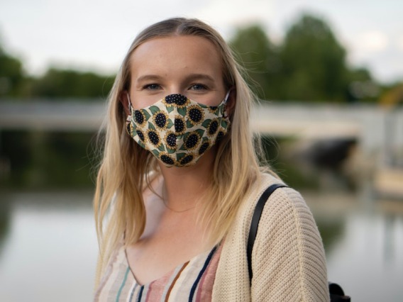 Woman in a mask in front of a lake.