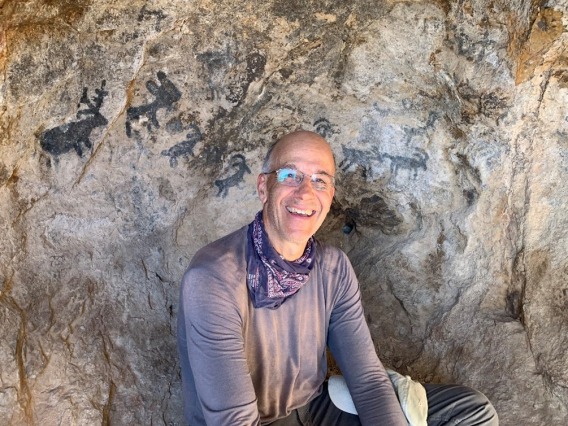 Bernard Futscher smiling int front of rock with ancient paintings on it.
