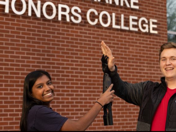 Two Biomedical Engineering Students holding up a prosthetic arm in a high-five motion.