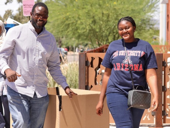 Student and their father walking towards camera with move-in equipment. 