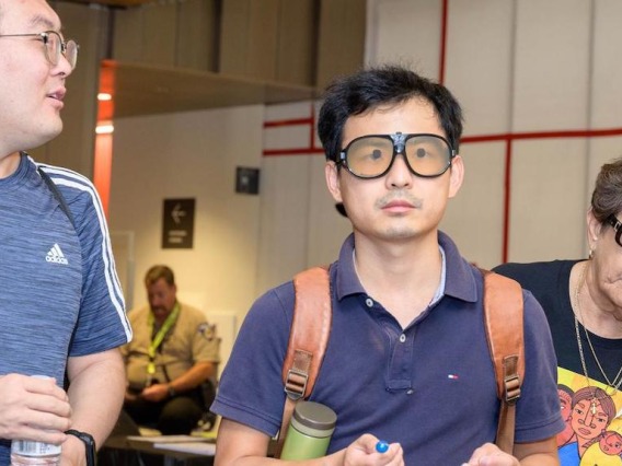 3 people in frame with one wearing special eyes glasses that simulate macular degenerative disease.