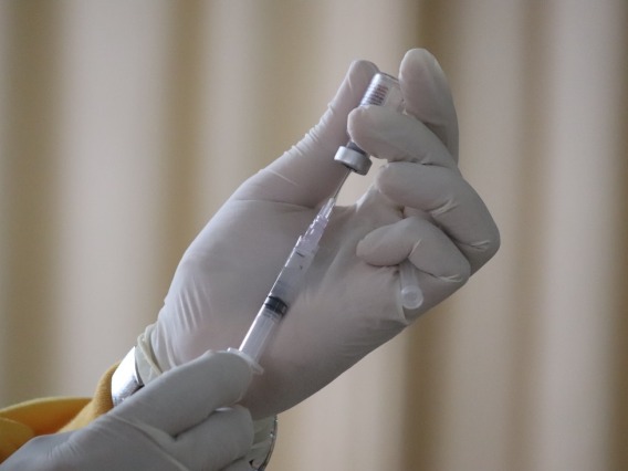 Gloved hand holding syringe with a needle injecting into a vile with a clear substance.