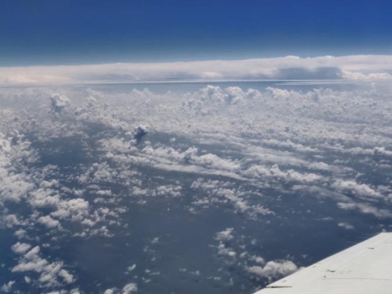 Arial view over the clouds with an airplane wing jetting into the image.