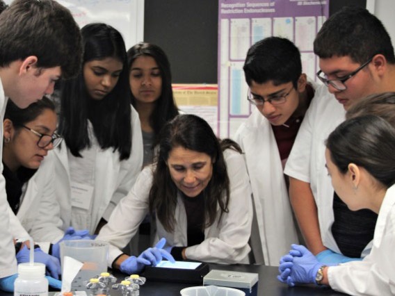 Group of students in lab coats gather around a scientist