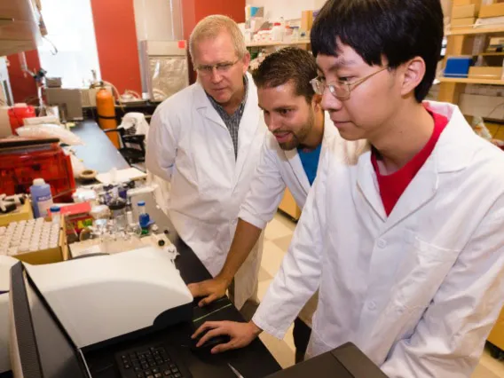 Student in lab coat works at a machine in laboratory