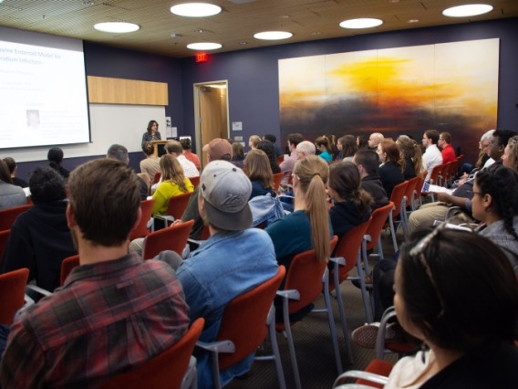 Crowd listens to a person presenting research at a podium