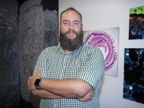 Person standing with arms crossed in front of a blackboard with chalk drawings and colorful scientific images on the wall.