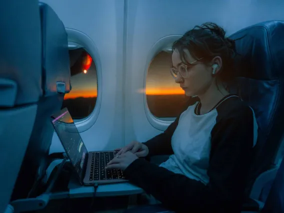 Person working on a laptop on a plane next to the window, with a sunset visible outside.