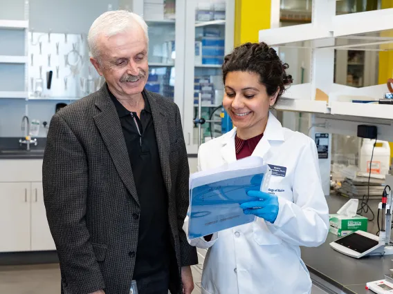 Two researchers, one holding a folder, smiling and discussing in a laboratory.