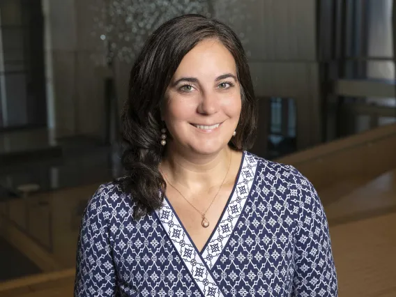 A person smiling in front of a darker background, whit a blue and white design shirt