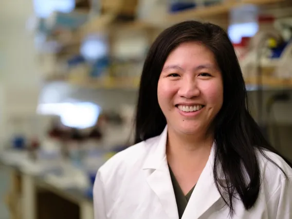 Person wearing a white lab coat smiling in a laboratory environment.