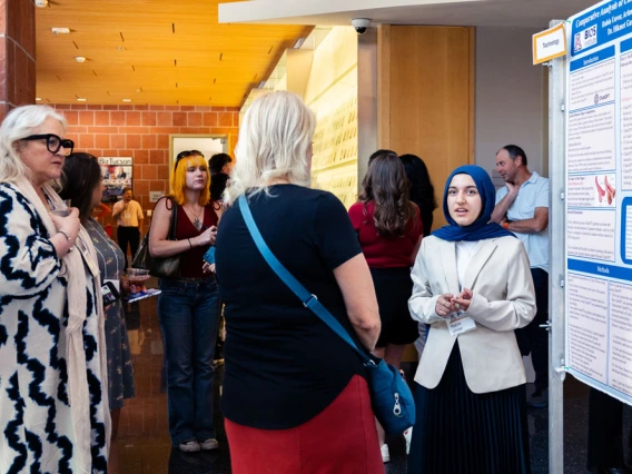 People conversing at a conference near informational posters, with one person wearing a hijab.