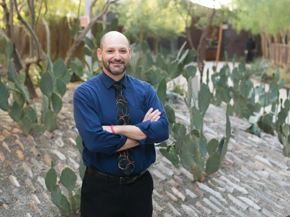 Person in a business casual outfit standing with crossed arms in front of a cactus garden.