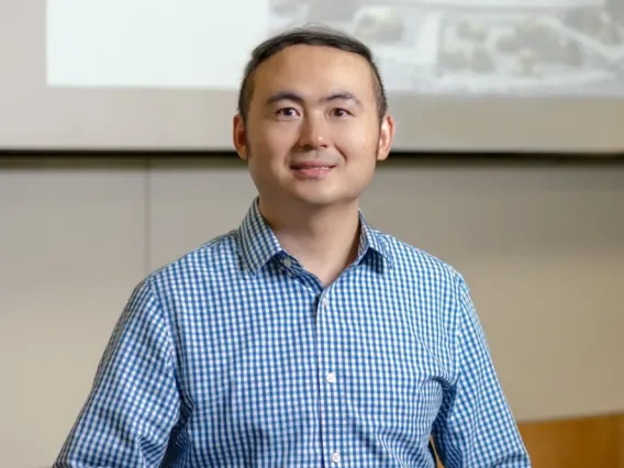 Image of Jianqin Lu smirking with blue collard shirt and whiteboard in background. 