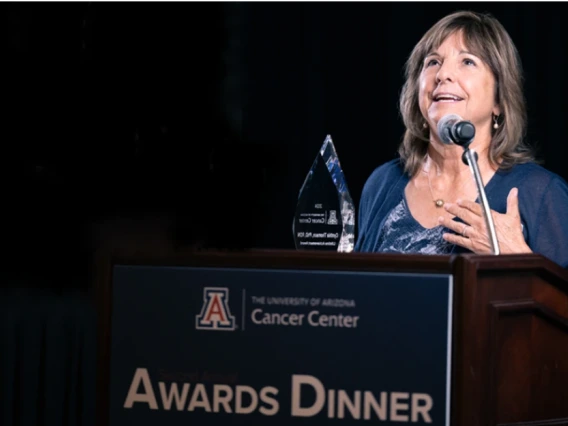 Person accepting an award at the University of Arizona Cancer Center Awards Dinner, standing at a podium with the event name visible.