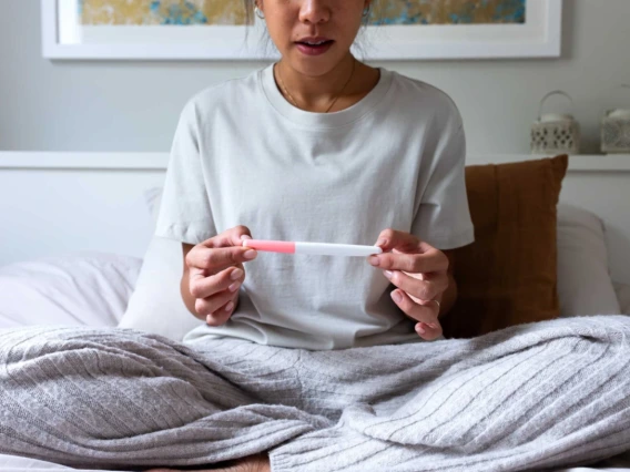 Person sitting on a bed, holding a pregnancy test, with a focused expression.