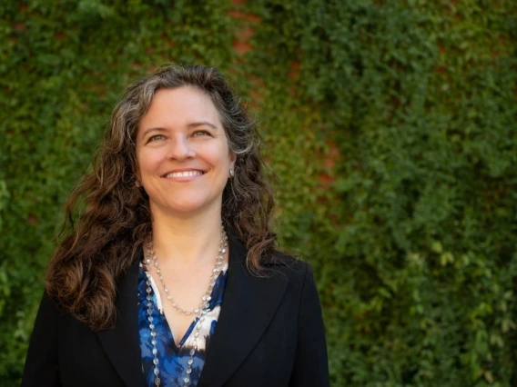 Person smiling in front of a lush green ivy-covered wall.
