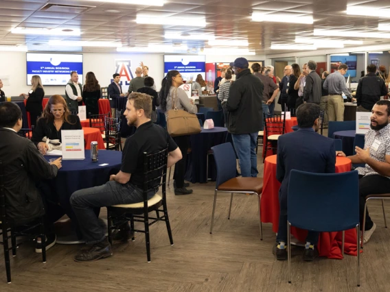 Attendees networking at a University of Arizona event in a conference room with tables, chairs, and promotional banners.