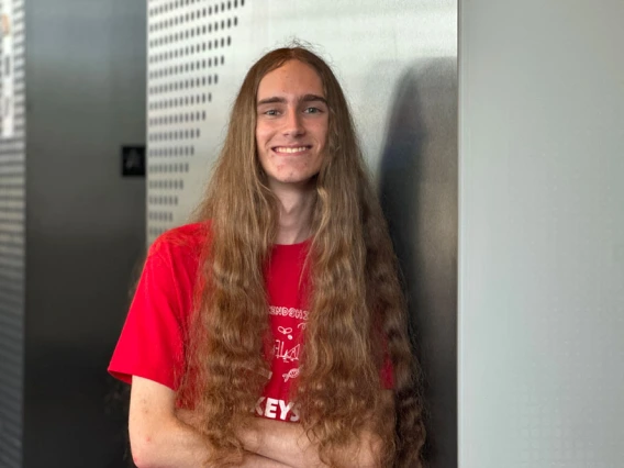 Young man with long hair wearing a red shirt stands confidently with his arms crossed