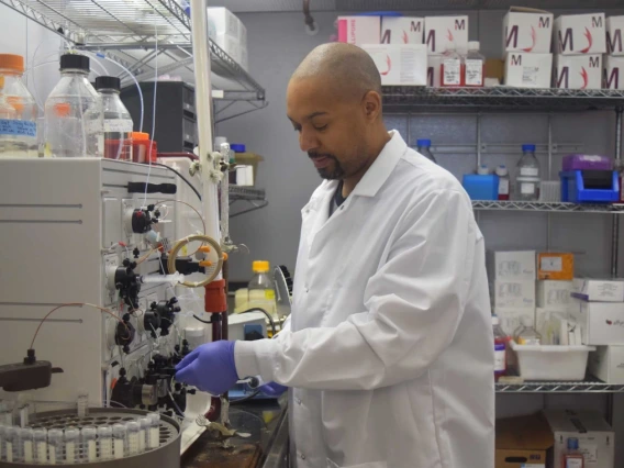 A scientist wearing a lab coat and gloves is working with samples in a centrifuge in a well-equipped laboratory.