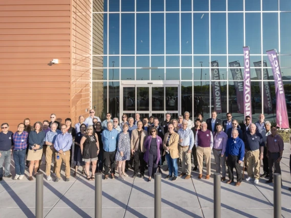 A group of people standing outside a modern building with glass façade and large banners reading "INNOVATION" and "COLLABORATION.