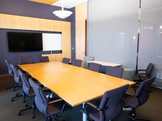 Modern conference room featuring a large wooden table, surrounded by swivel chairs, and equipped with a widescreen TV on the wall.