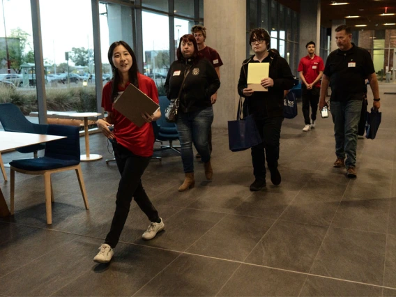 Group of five individuals walking through a modern lobby, carrying notebooks and wearing lanyards.