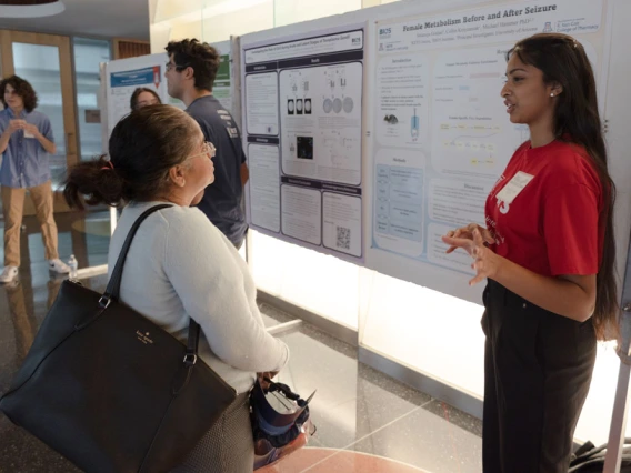 Two individuals discussing a scientific poster presentation at an event. Other attendees are visible in the background.
