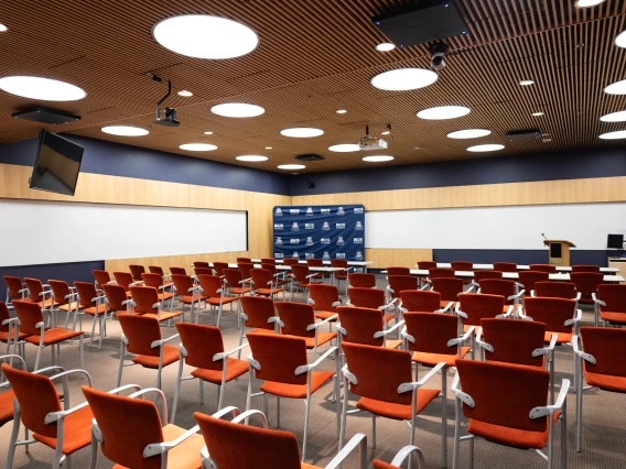 A conference room with rows of red chairs facing a podium, whiteboard, and a banner with BIO5 logos in the background.