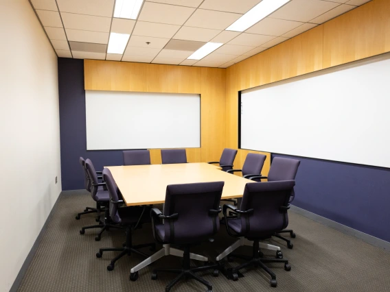 Empty conference room with a large table, several chairs, and two blank whiteboards on the walls.
