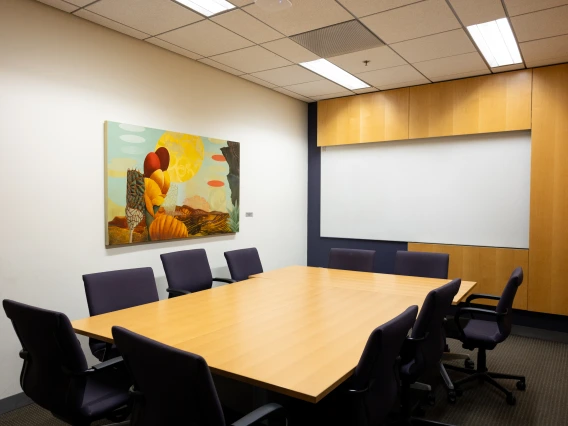 Boardroom with a large wooden table surrounded by black office chairs and a colorful abstract painting on the wall.