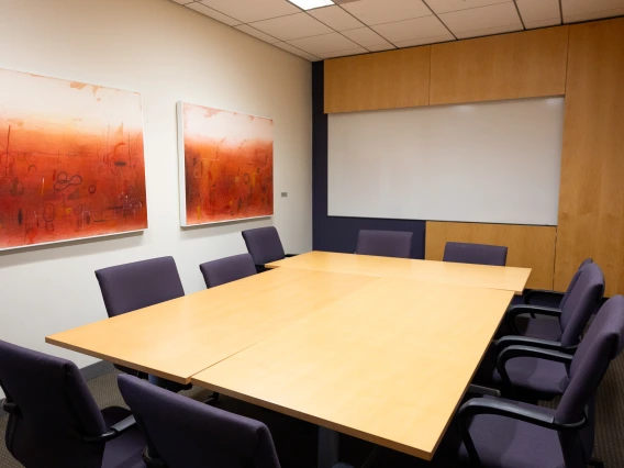 Conference room with a large table surrounded by office chairs, two abstract paintings on the wall, and a whiteboard.
