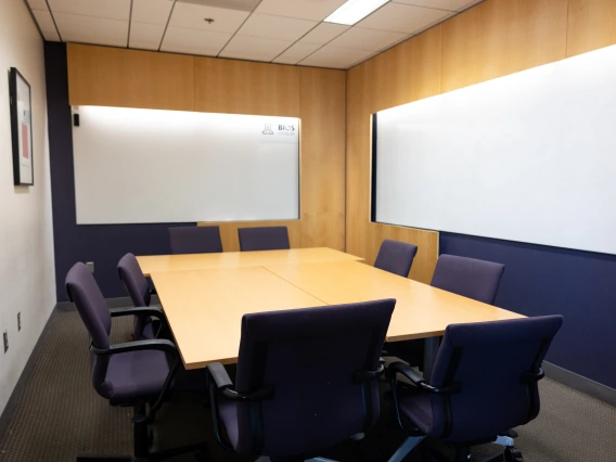 Conference room with a large table surrounded by blue office chairs and two whiteboards on the walls.