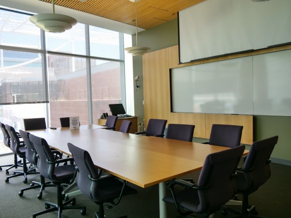 Modern conference room with a large oval table, several chairs, and a whiteboard in a well-lit interior space.