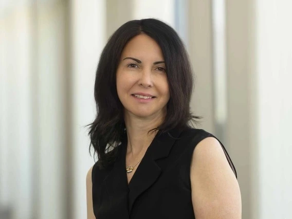 Portrait of a professional in a black sleeveless top, standing indoors with a soft focus background.