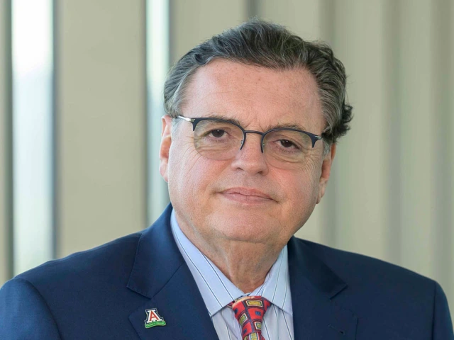 Portrait of a person wearing a suit with a University of Arizona lapel pin, standing indoors.