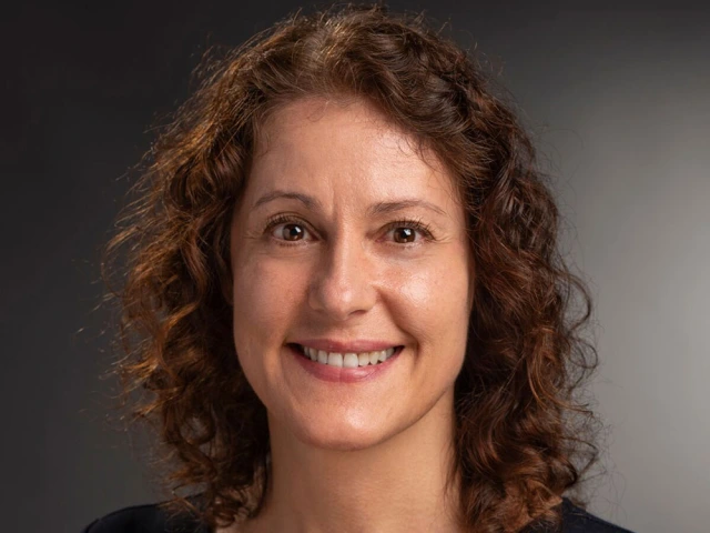 Professional headshot of a smiling individual with curly hair, wearing a navy blue top.